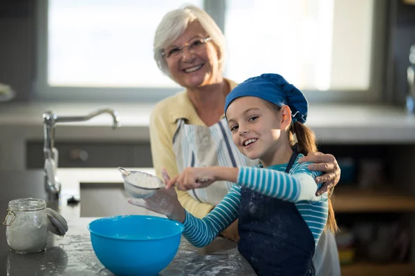 Nonna posa con nipote setacciare farina — Foto Stock