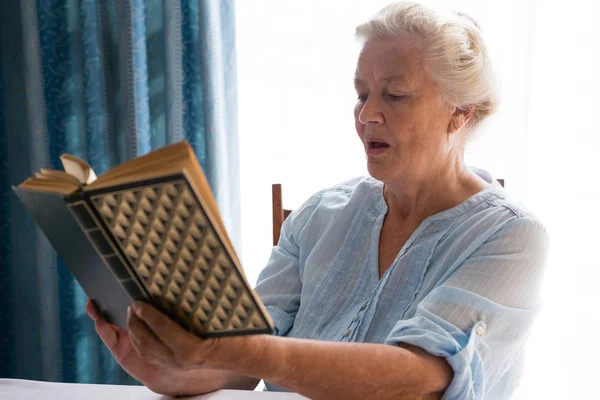 Seniorin liest Buch, während sie am Tisch sitzt — Stockfoto