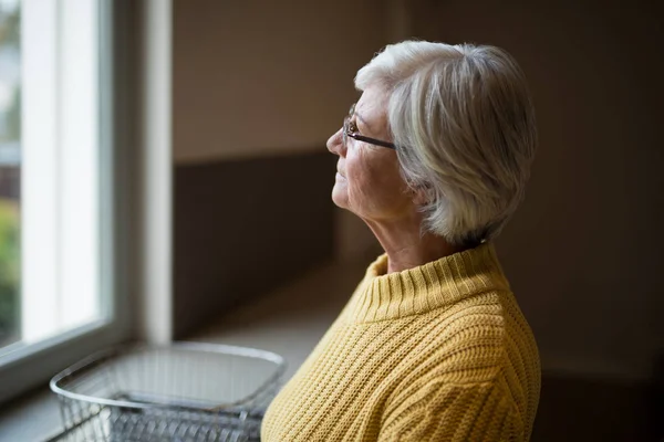 Przemyślane starszy kobieta patrząc przez okno — Zdjęcie stockowe