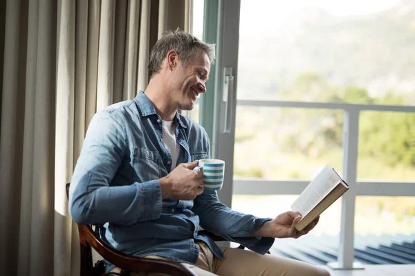 Чоловік читає книгу, маючи каву — стокове фото