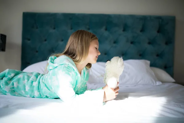 Chica sosteniendo oso de peluche en la cama en el dormitorio —  Fotos de Stock