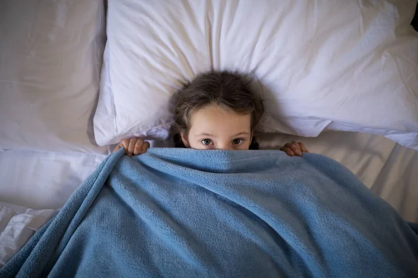 Meisje die betrekking hebben op haar gezicht onder de deken — Stockfoto