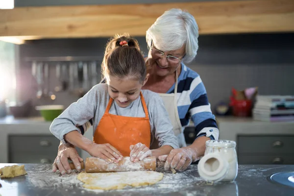 Grandmother helping granddaughter to flatten dough — Stock Photo, Image