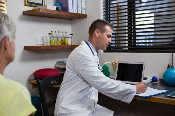 Fisioterapeuta escribiendo prescripción en portapapeles para el paciente — Foto de Stock