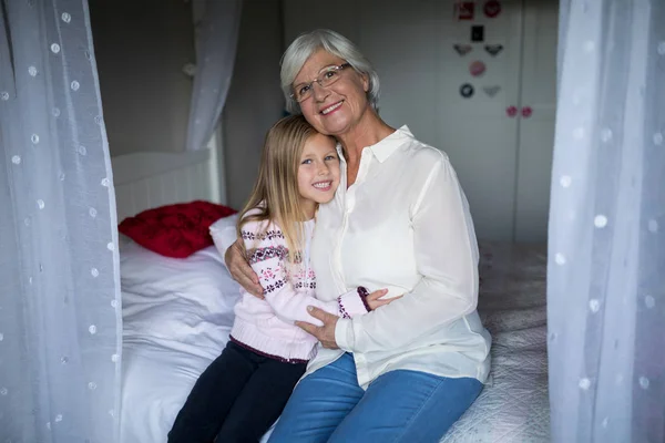 Grandmother and granddaughter sitting together on bed — Stock Photo, Image