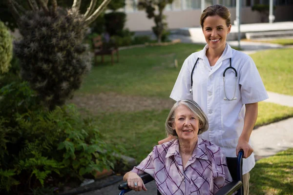 Médico em pé por mulher idosa na cadeira de rodas — Fotografia de Stock