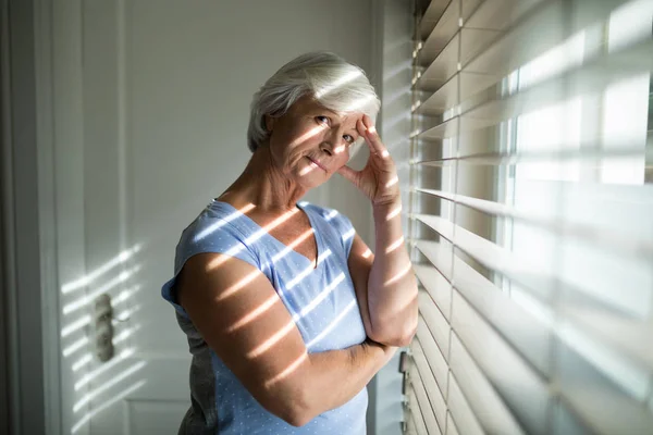 Напряженная пожилая женщина, стоящая у окна — стоковое фото