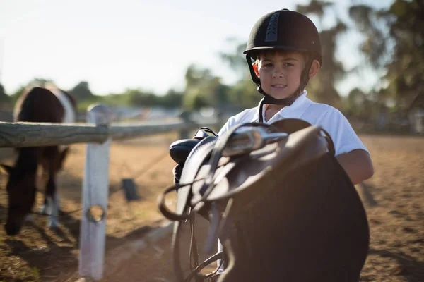 Garçon tenant une selle de cheval — Photo