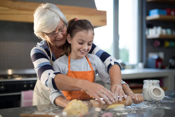 Grandmother helping granddaughter to flatten dough — Stock Photo, Image