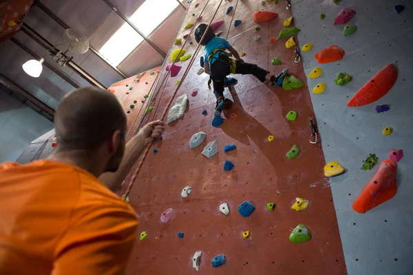 Trainer assisting boy in rock climbing — Stock Photo, Image