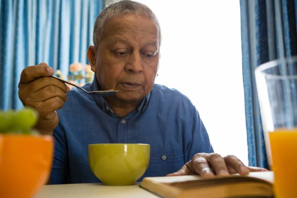 Старший мужчина ест за чтением книги — стоковое фото