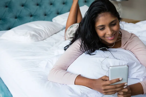 Leende kvinna med telefonen på sängen — Stockfoto