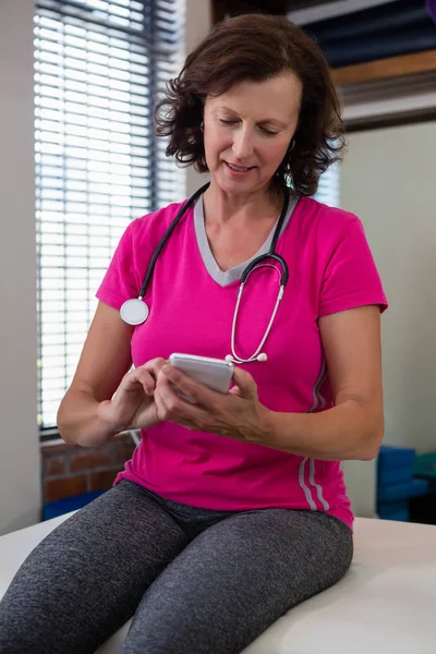 Sjukgymnast med mobiltelefon på säng — Stockfoto