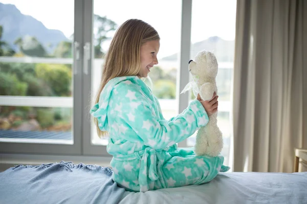 Chica sosteniendo oso de peluche en la cama en el dormitorio —  Fotos de Stock