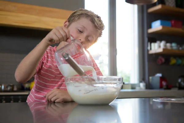 Niño vertiendo leche en masa en la cocina —  Fotos de Stock