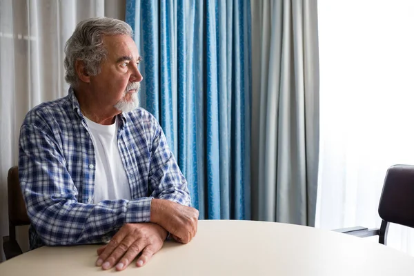 Nachdenklicher Senior sitzt am Tisch — Stockfoto