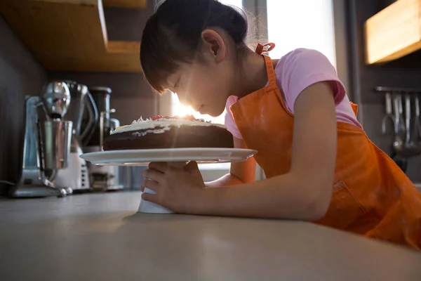 Menina olhando para bolo de creme na cozinha — Fotografia de Stock