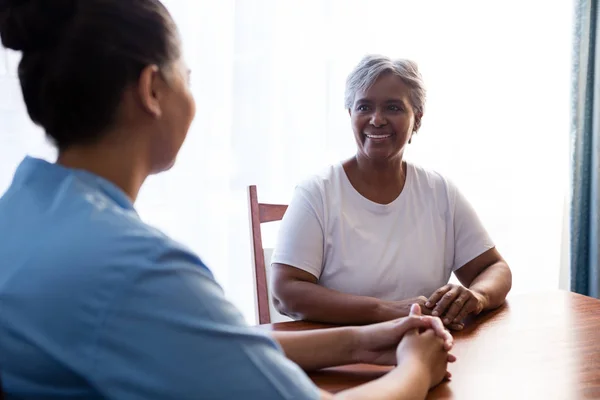 Verpleegkundige interactie met senior vrouw aan tafel — Stockfoto