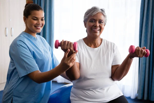 Perawat membantu wanita senior mengangkat dumbbells — Stok Foto
