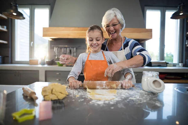 Grandmother helping granddaughter to flatten dough — Stock Photo, Image