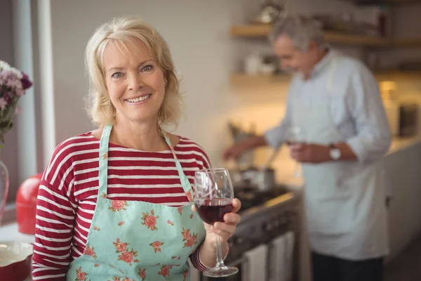 Senior woman holding glass of wine in kitchen — Stock Photo, Image
