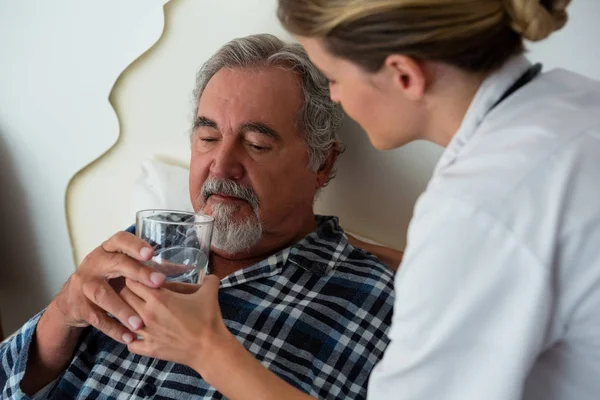 Kvinnliga läkare som ger vatten till senior patient — Stockfoto