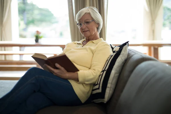 Старша жінка читає книгу на дивані у вітальні — стокове фото