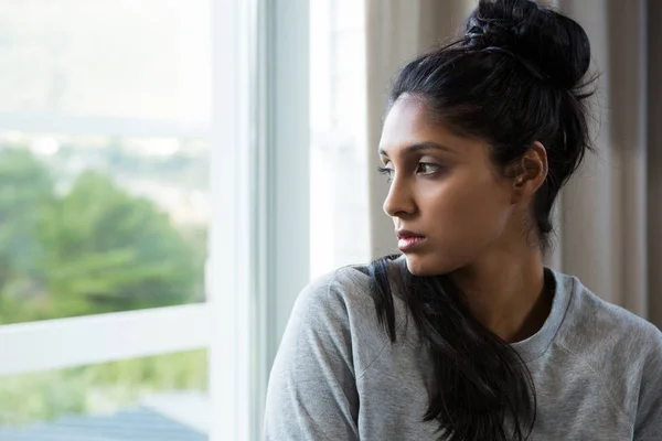 Thoughtful young woman by window — Stock Photo, Image