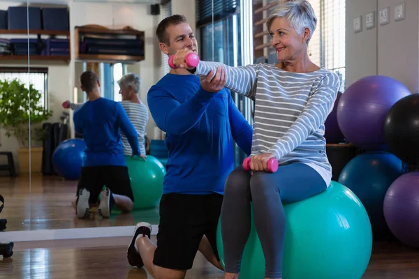 Fisioterapeuta auxiliando a mulher idosa na bola de exercício — Fotografia de Stock
