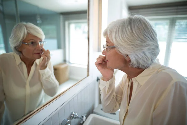 Femme âgée vérifiant sa peau dans le miroir — Photo