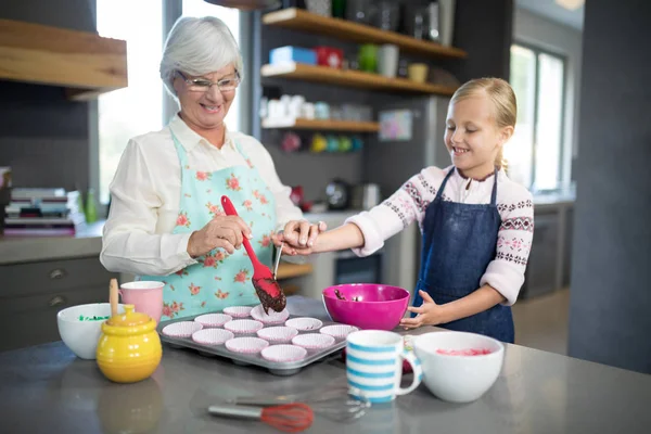 Бабушка помогает внучке наливать кексовое тесто — стоковое фото