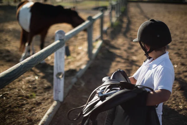 Garçon tenant une selle de cheval — Photo