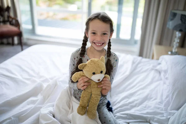 Chica sosteniendo oso de peluche en la cama en el dormitorio —  Fotos de Stock