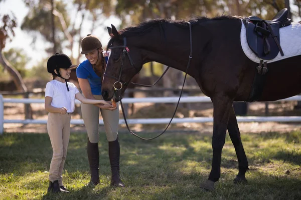 Jóquei feminino com a irmã alimentando cavalo — Fotografia de Stock