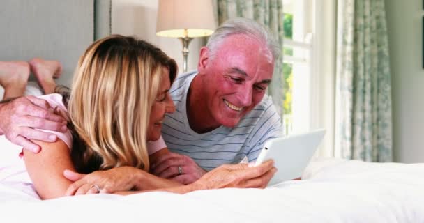 Пара лежить на ліжку і використовує цифровий планшет — стокове відео