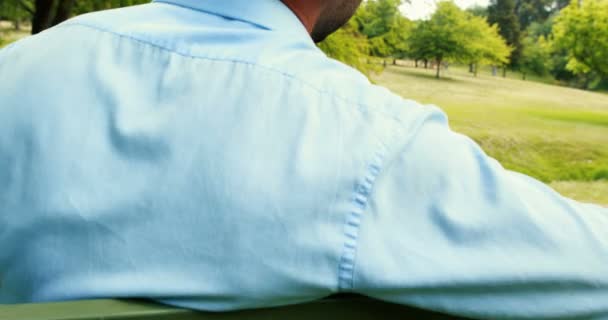 Mannen sitter på bänken i parken — Stockvideo