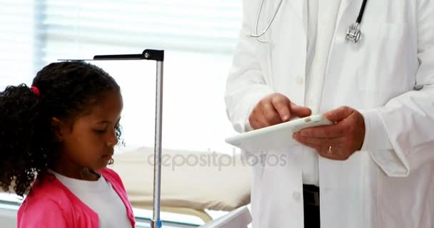 Médico usando tableta digital mientras mide la altura de la niña — Vídeos de Stock