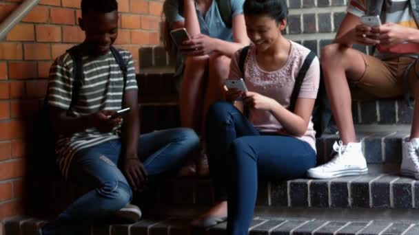 Mitschüler sitzen im Treppenhaus und nutzen Mobiltelefone — Stockvideo