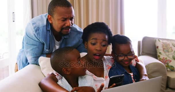 Padres e hijos usando laptop y smartphone en sofá — Vídeo de stock