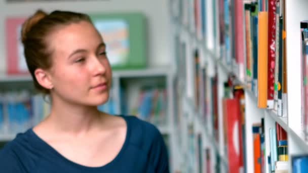 Colegiala seleccionando libro de estante de libro en la biblioteca — Vídeo de stock