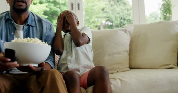 Son covering his eyes while watching television with father — Stock Video