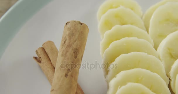 Plátanos en rodajas y palitos de canela en plato — Vídeos de Stock