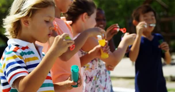 Les écoliers jouent avec la baguette à bulles dans l'aire de jeux — Video