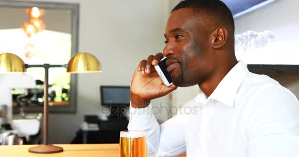 Hombre hablando en el teléfono móvil mientras toma cerveza en el mostrador — Vídeo de stock