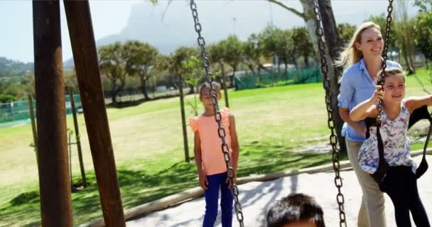 Trenér tlačí schoolkids na houpačce na hřišti — Stock video