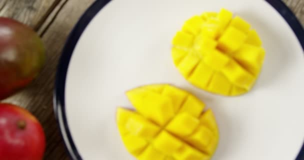 Halved and chopped mango with glass of water on wooden table — Stock Video