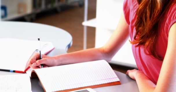 Внимательная школьница делает домашнее задание в библиотеке — стоковое видео