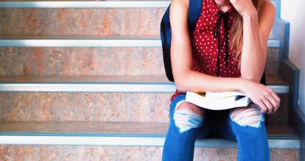 Sad schoolgirl sitting alone on staircase — Stock Video