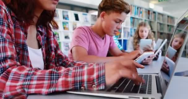 Школьники, использующие ноутбук и цифровой планшет в библиотеке — стоковое видео