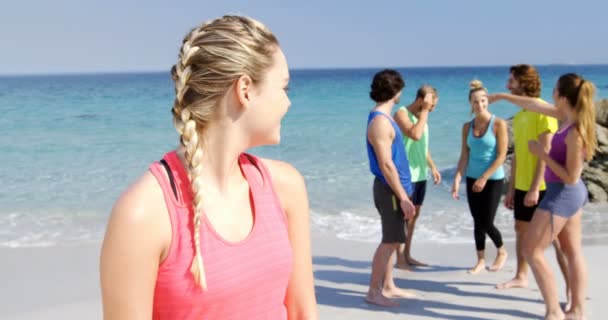 Fitte Frau lächelt in die Kamera, während Freunde hinter ihr am Strand interagieren — Stockvideo